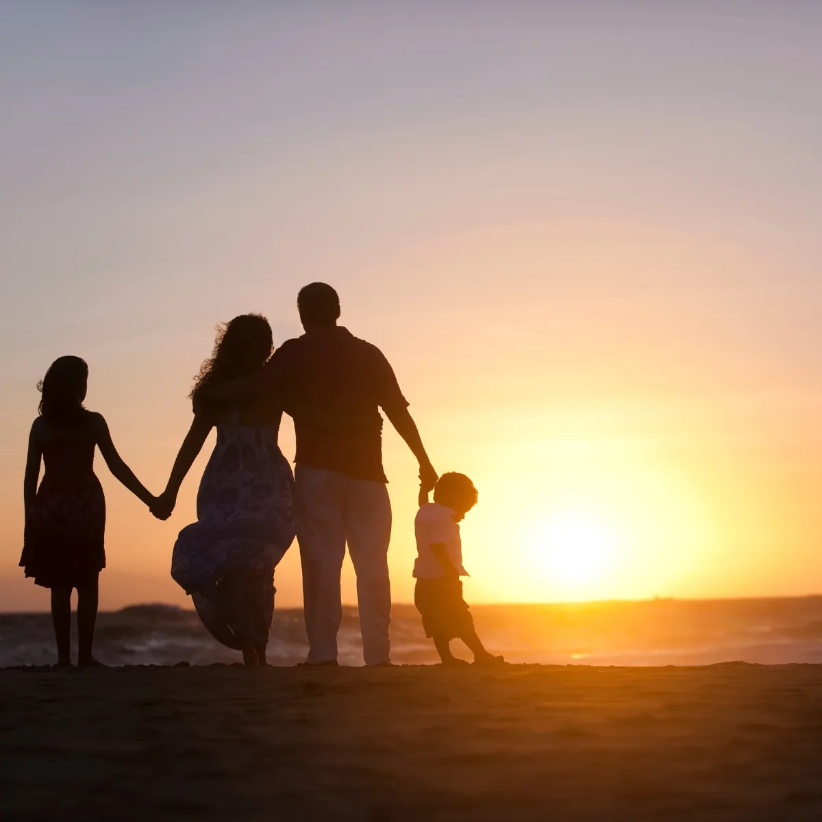 A family holding hands on the beach at sunset, silhouetted against golden light
